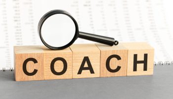 wooden blocks with the text: coach with magnifying glass. coach word made with building wooden blocks. can be used for business, marketing and education concept
